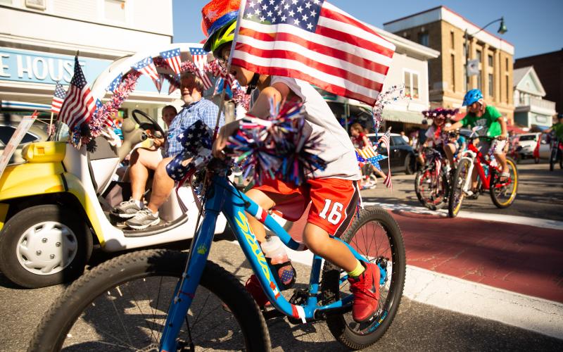 Kid rides bike with an American flag in the Lake Placid July 4th Parade