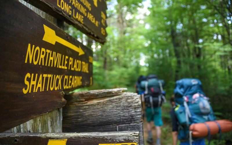 A trail sign that reads Northville Placid Trail in front of hikers wearing large packs