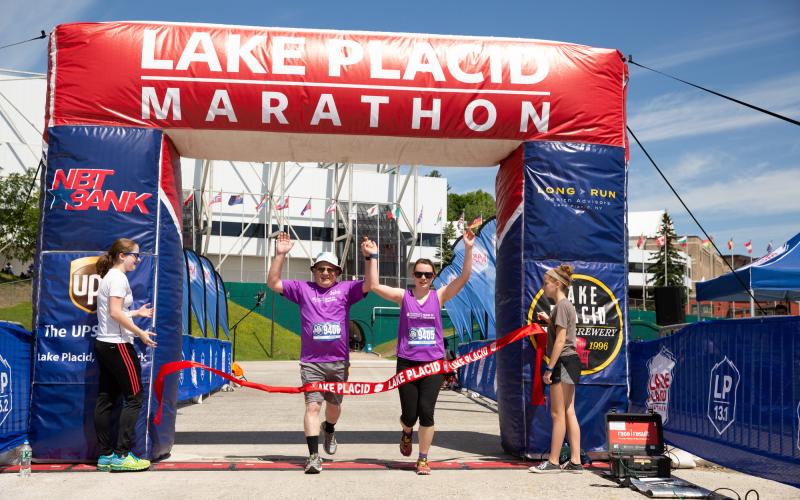 Two athletes cross the finish line holding hand in the air