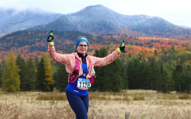 Female racer gives two thumbs up as she run with fall foliage in the background