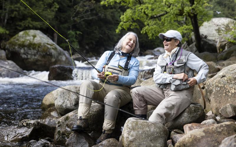 Two fisherwomen laugh on banks of river