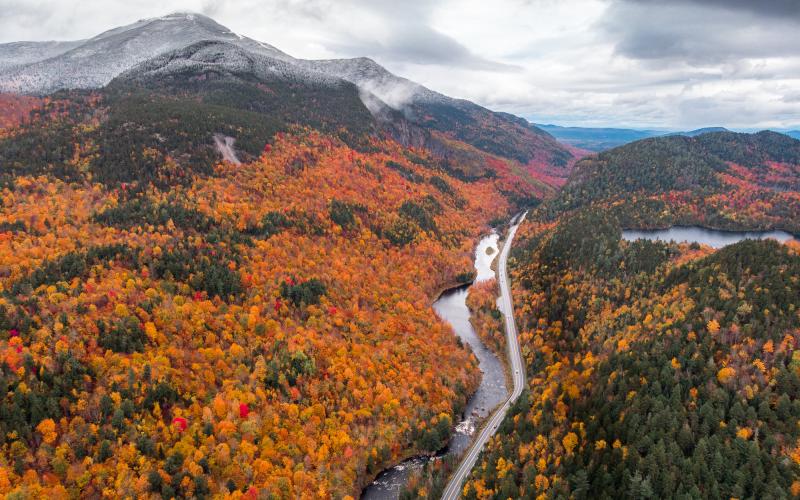 An aerial view of a snow-touched mountain and fall colored trees
