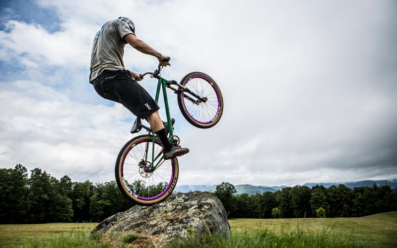mountain biker pops up on their back wheel on a rock in a field at the Craig Wood Trails