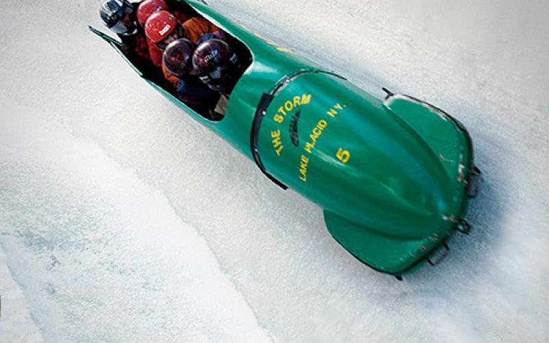 A group of five riding a green bobsled on an icy track.
