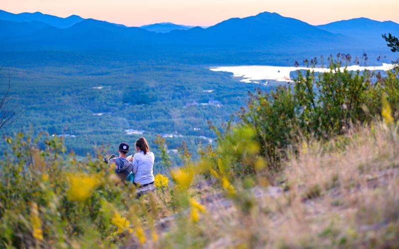 A couple stares out at the silhouette of the high peaks in the Adirondacks from the summit of Haystack Mountain during sunsetHaystack Mountain