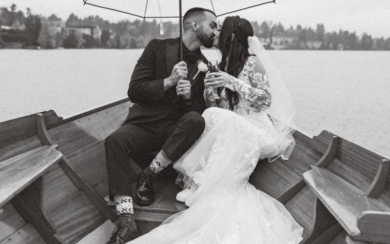 Black and white photo of the bride and groom kissing under an umbrella in the rain