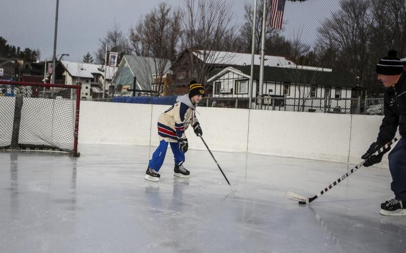 A father and son play hockey at a small rink