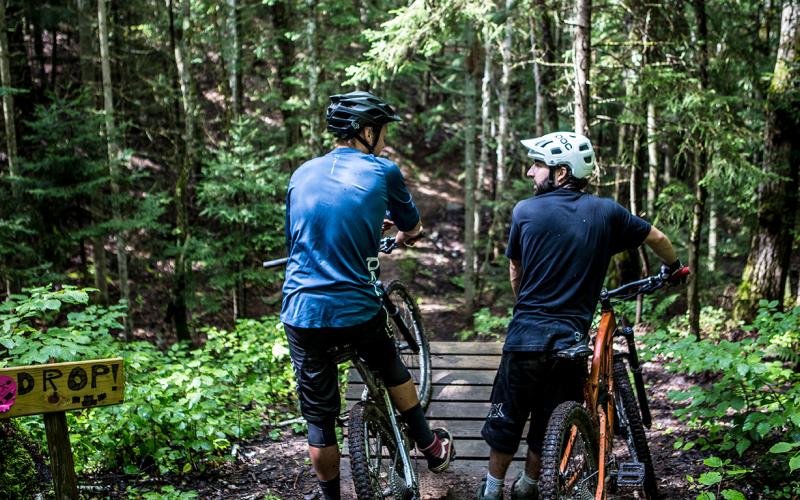 A pair of mountain bikers take a break before crossing a mountain biking bridge.