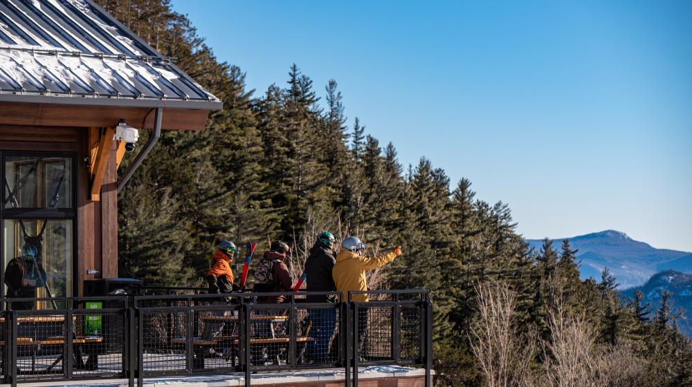 A group of skiing friends looks at the mountain range from a lodge patio.