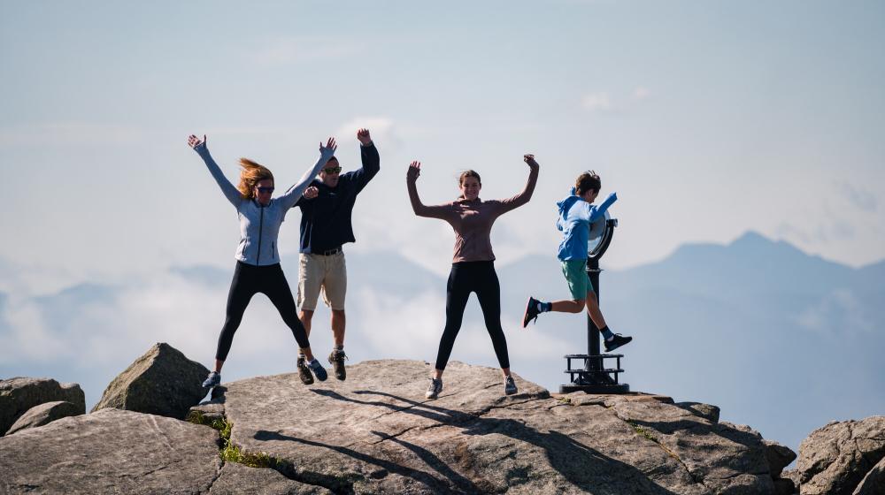 Four people jump into the air on top of a mountain