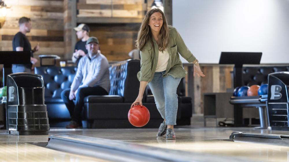 A woman rolls a bowling ball down a lane.